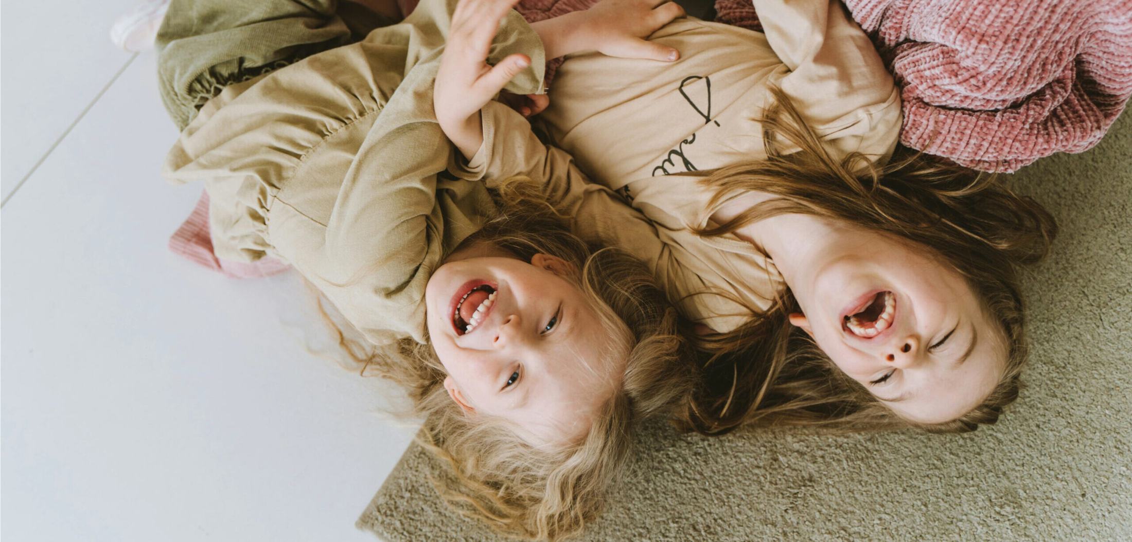 Due bambine che ridono, sdraiate sul pavimento